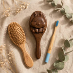 Wooden hairbrush, rabbit-shaped brush, and bamboo toothbrush on a textured surface with flowers and leaves.