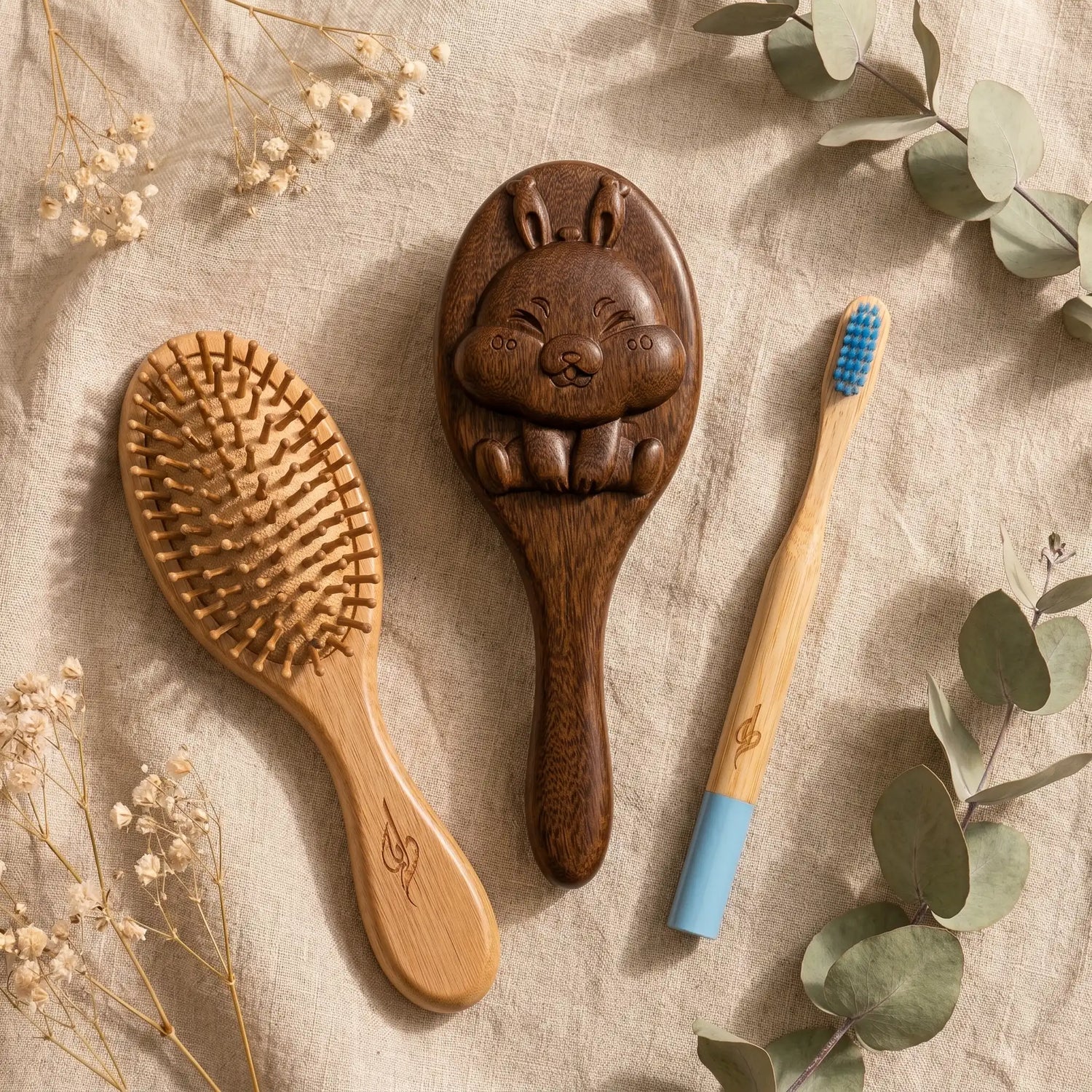 Wooden hairbrush, rabbit-shaped brush, and bamboo toothbrush on a textured surface with flowers and leaves.