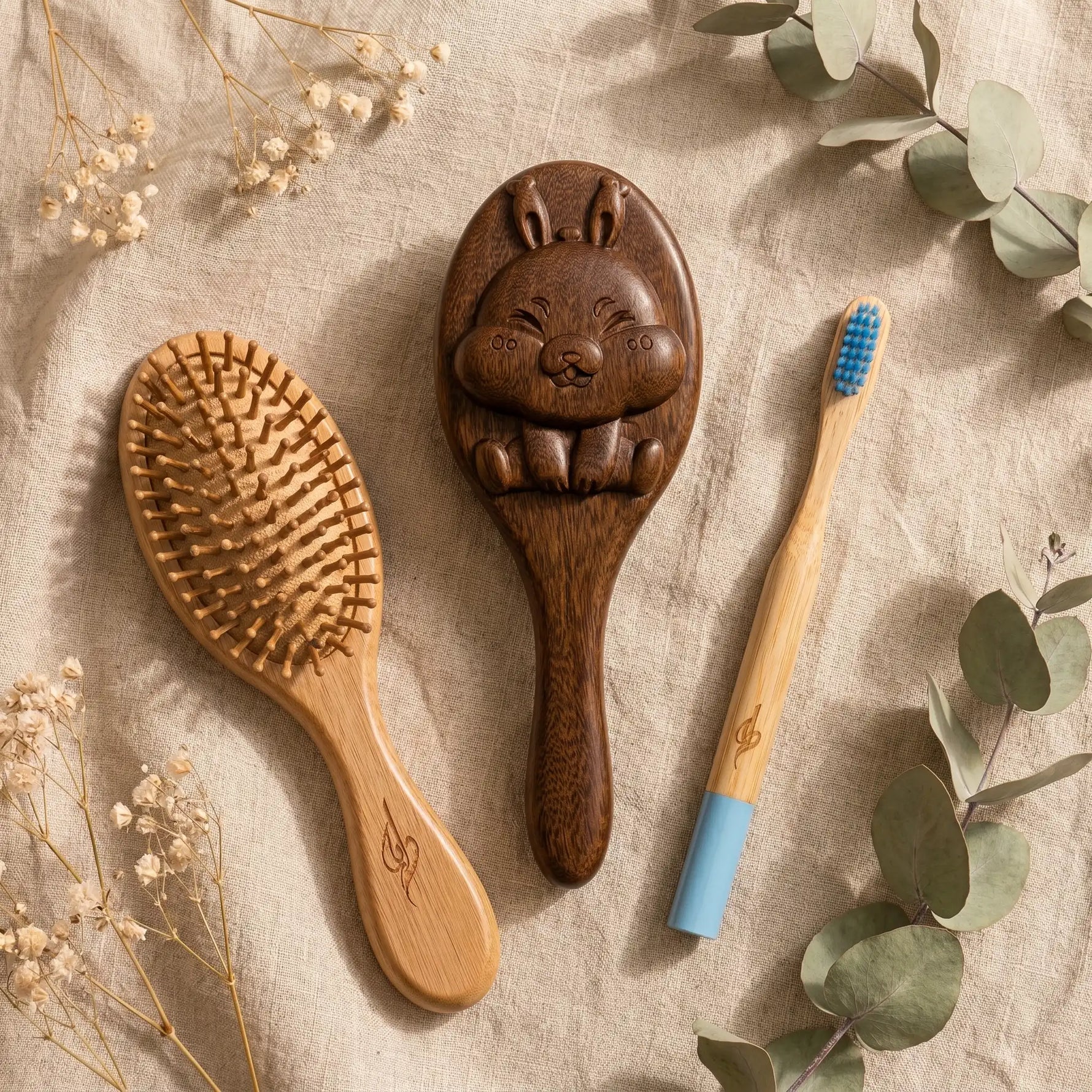 Wooden hairbrush, rabbit-shaped brush, and bamboo toothbrush on a textured surface with flowers and leaves.