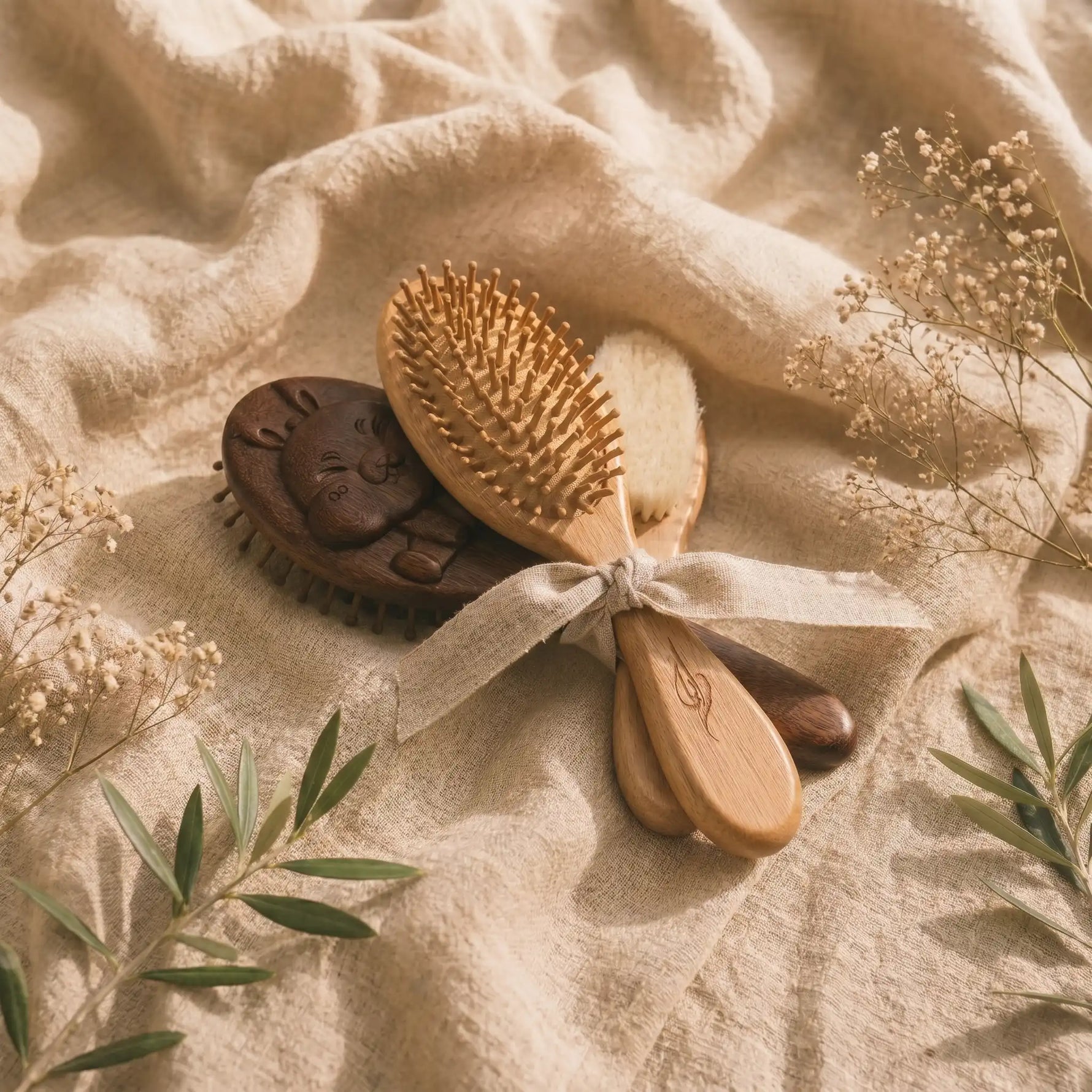 Two wooden hairbrushes with a ribbon on a textured fabric background with dried flowers and leaves.