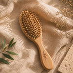 Bamboo hairbrush on a textured beige fabric background with dried flowers and leaves.