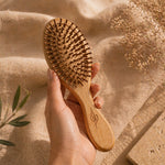Hand holding a Bamboo hairbrush against a textured beige background