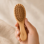 Hand holding a Bamboo kids hairbrush against a beige background