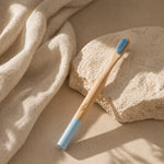 Bamboo toothbrush with blue bristles on a beige stone surface
