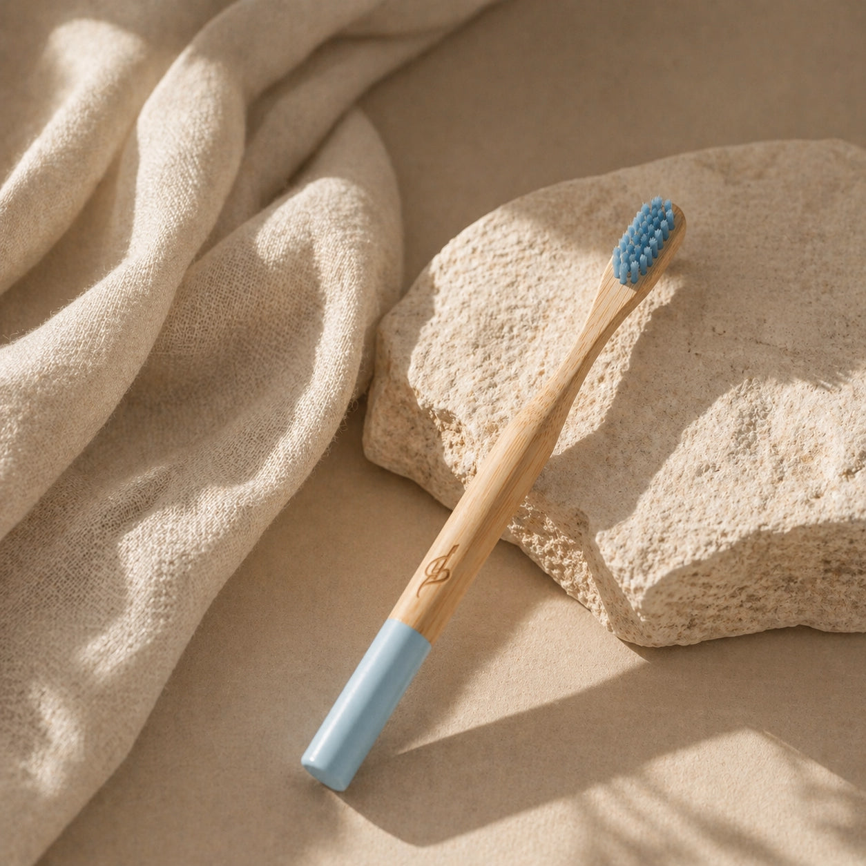 Bamboo toothbrush with blue bristles on a beige stone surface