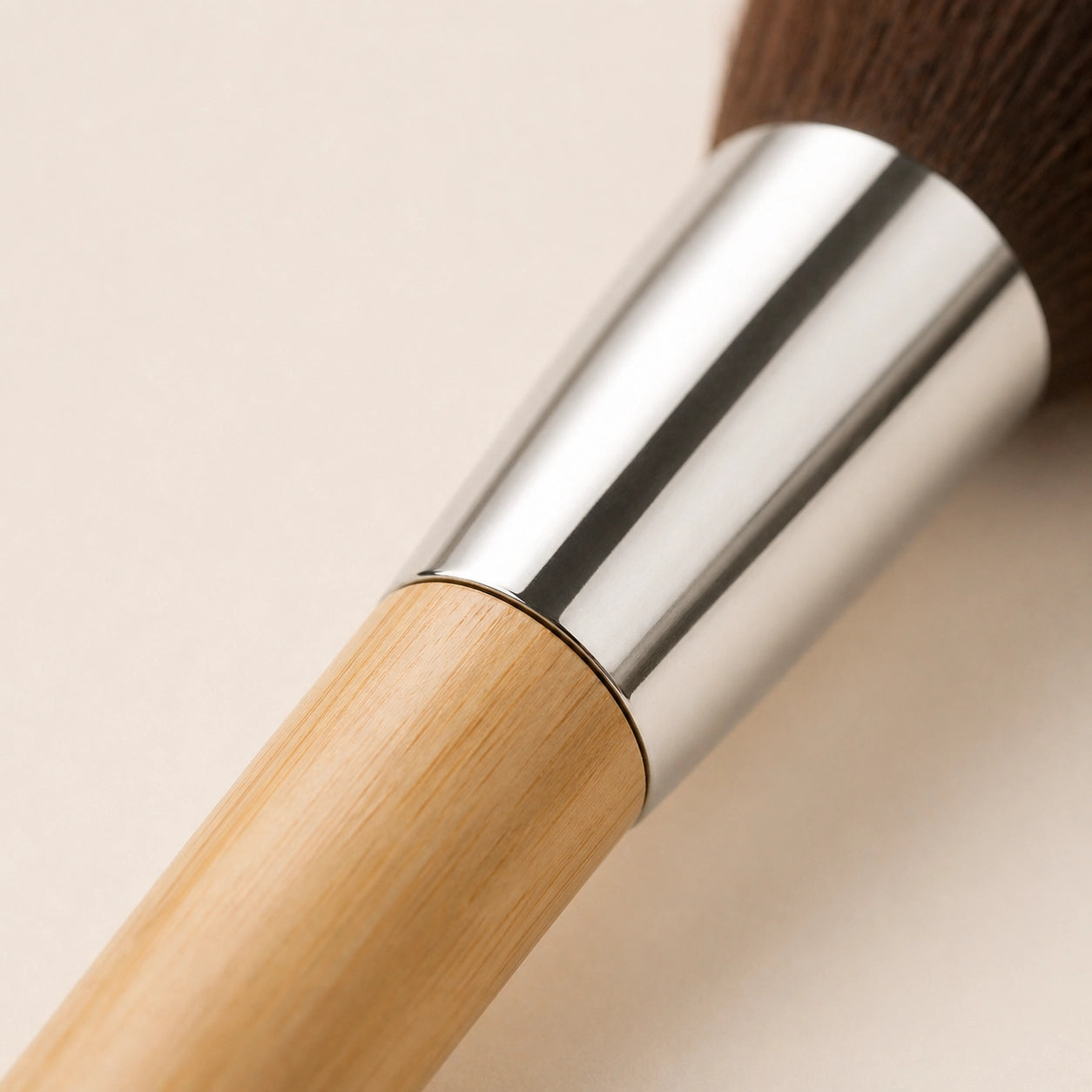Makeup brush with bamboo wooden handle and silver ferrule on a beige background