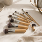 Set of makeup brushes with bamboo wooden handles on a light surface.