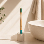 Bamboo toothbrush with green bristles in a white holder on a beige surface.