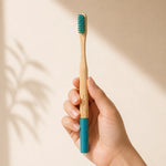 Hand holding a bamboo toothbrush with a blue handle and bristles on a beige background
