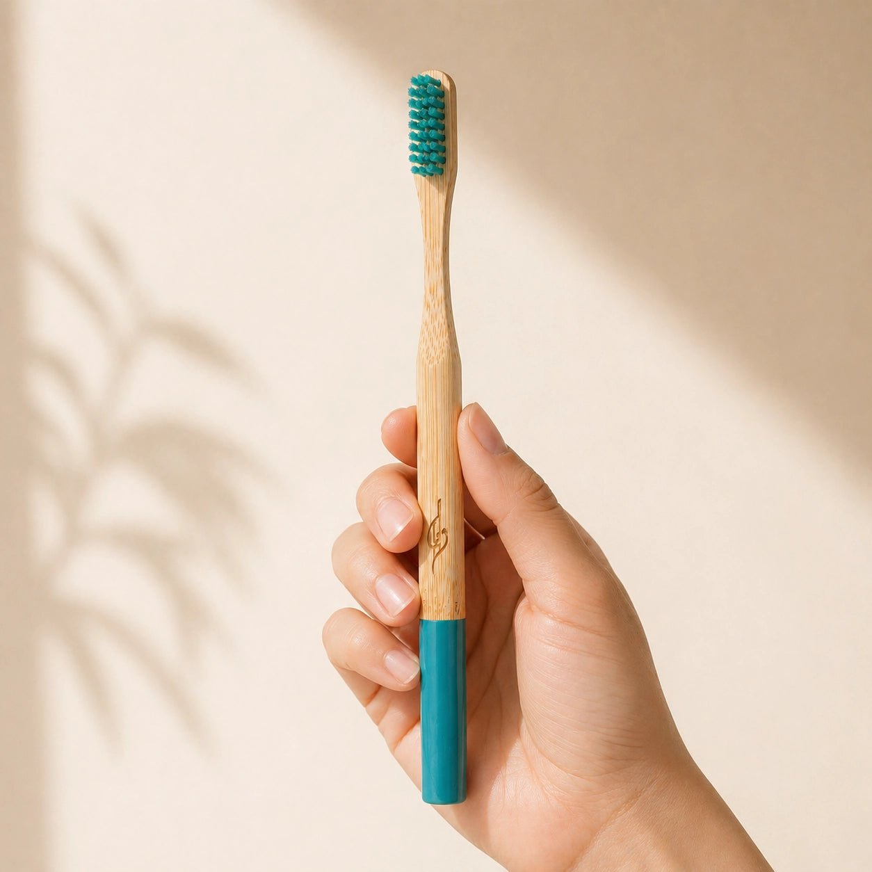 Hand holding a bamboo toothbrush with a blue handle and bristles on a beige background