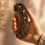 Hand holding a intricately carved sandalwood comb with a blurred natural background