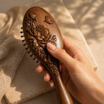 sandalwood hairbrush with floral patterns held by a hand against a beige fabric background