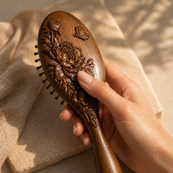 sandalwood hairbrush with floral patterns held by a hand against a beige fabric background