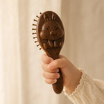 sandalwood hairbrush with animal design held by a hand against a beige background
